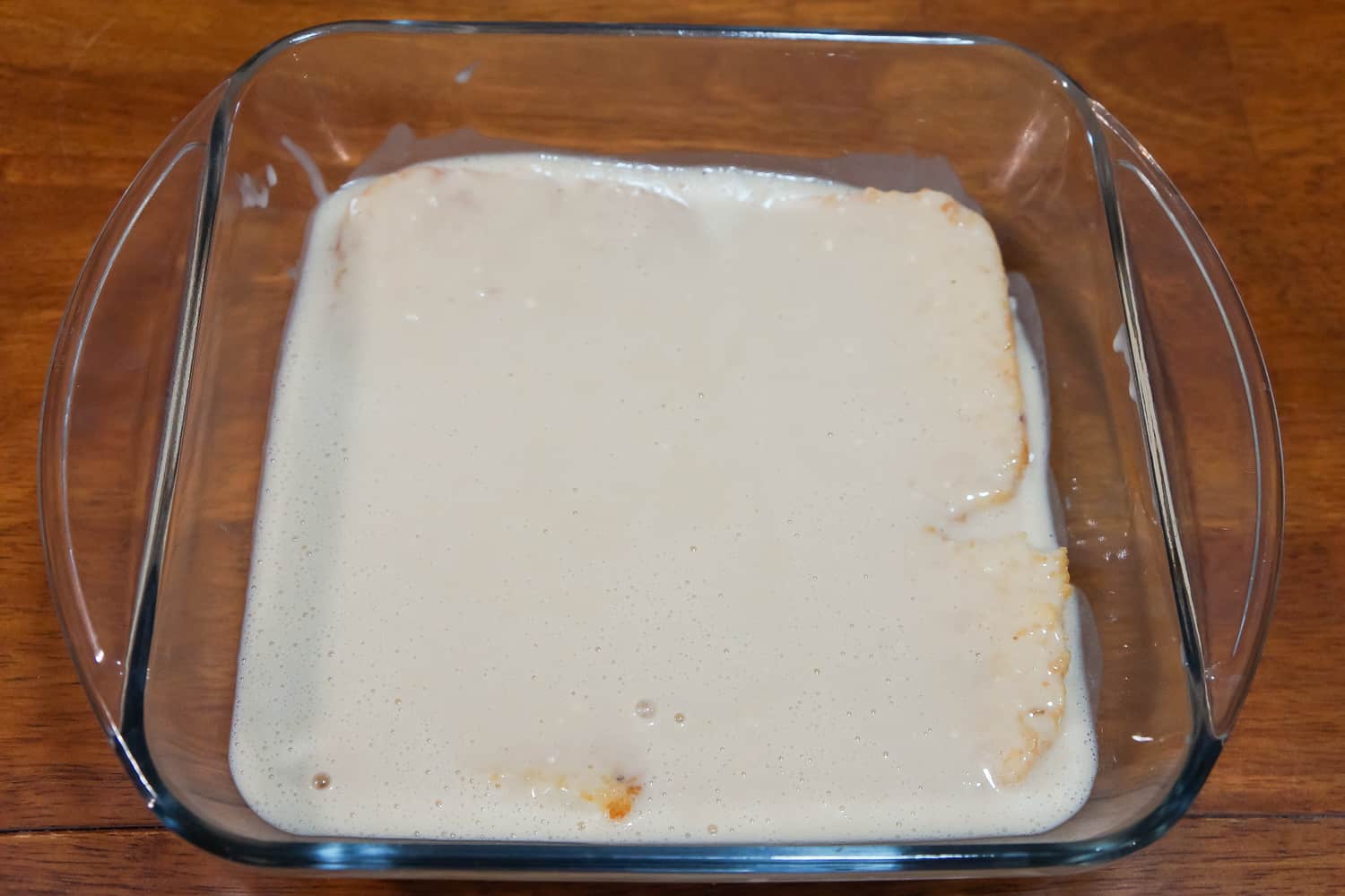 pancake mixture on top of frozen hash brown patties in a baking dish