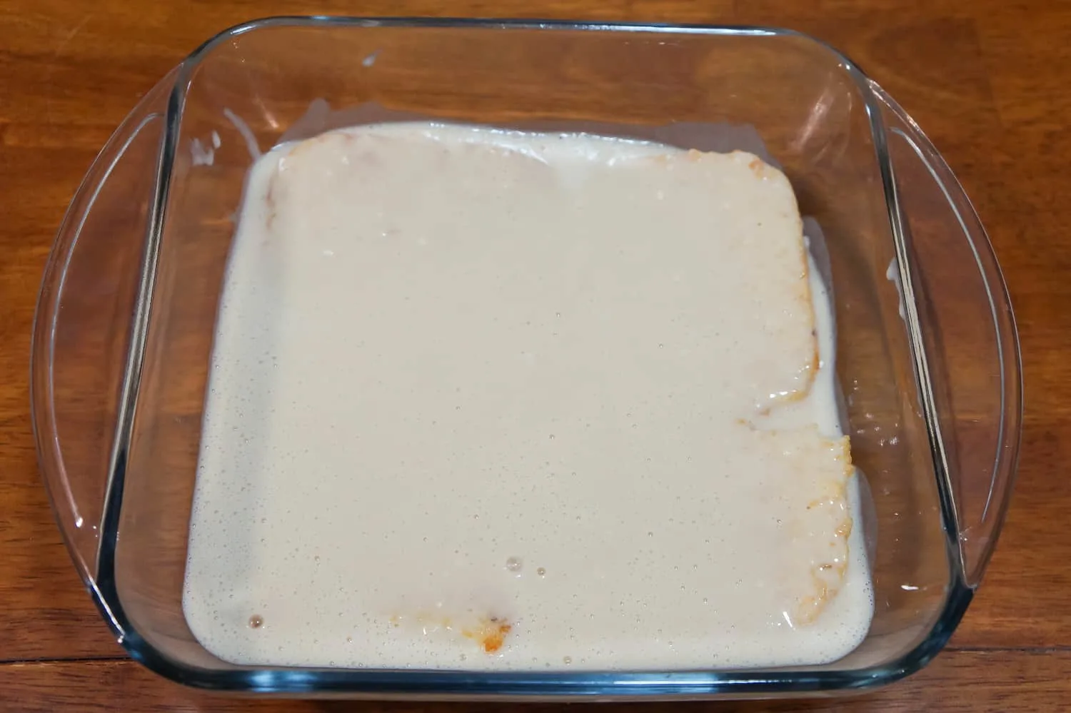 pancake mixture on top of frozen hash brown patties in a baking dish