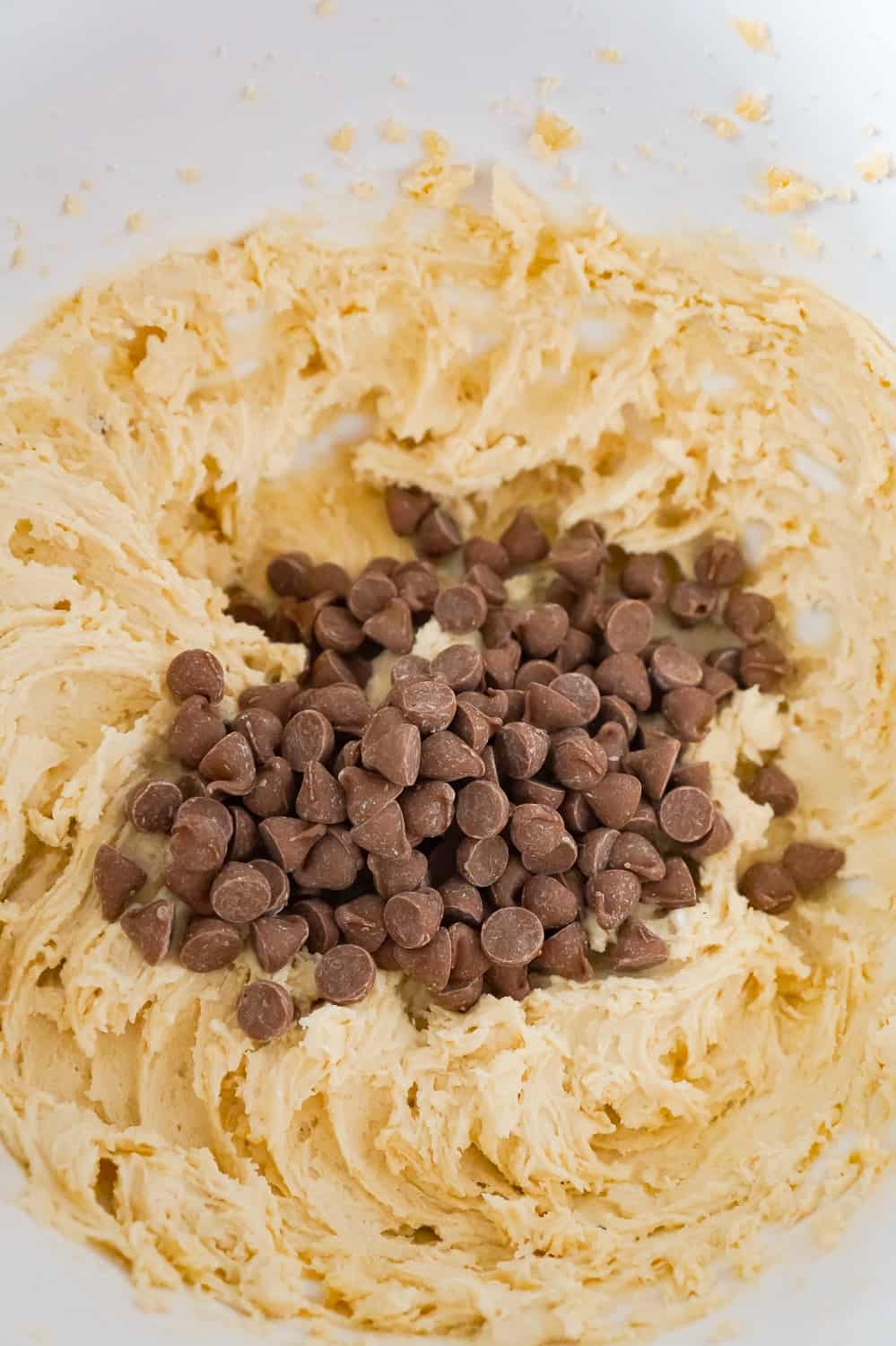 milk chocolate chips on top of cookie dough in a mixing bowl