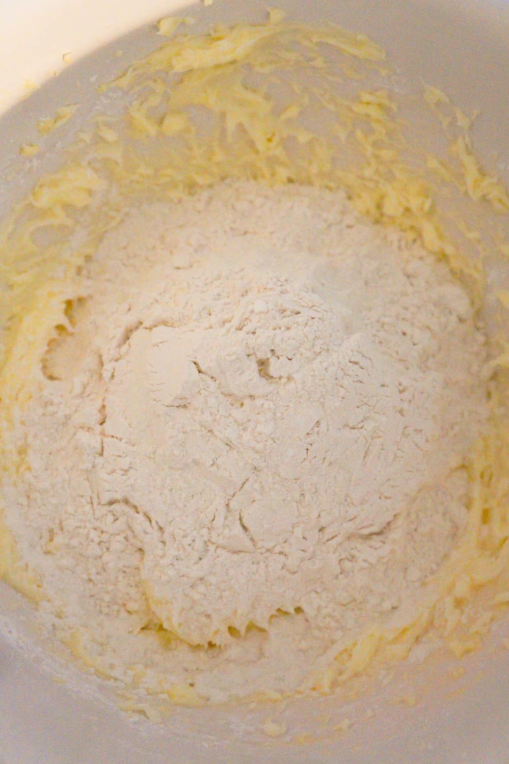 all purpose flour on top of icing sugar, butter and egg white mixture in a mixing bowl