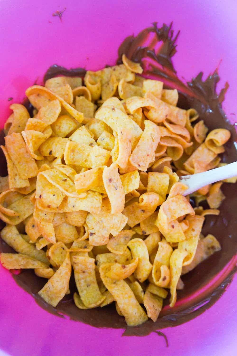 Fritos corn chips on top of melted chocolate in a mixing bowl