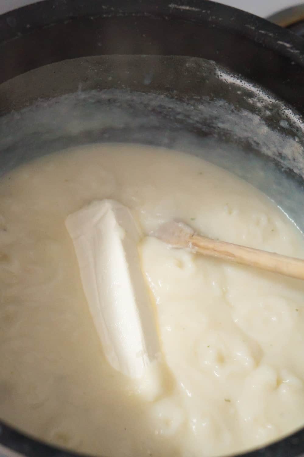 a brick of cream cheese in a pot of potato soup