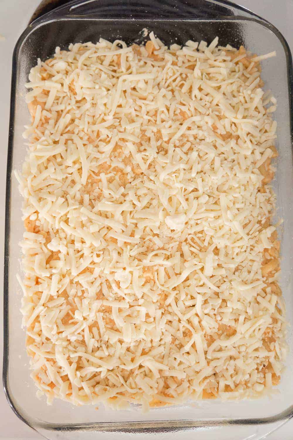 shredded mozzarella cheese on top of macaroni and cheese in a baking dish