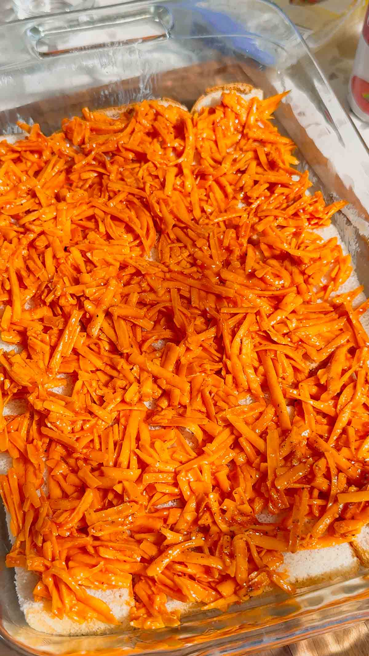 shredded cheddar cheese mixture on top of bread in a baking dish
