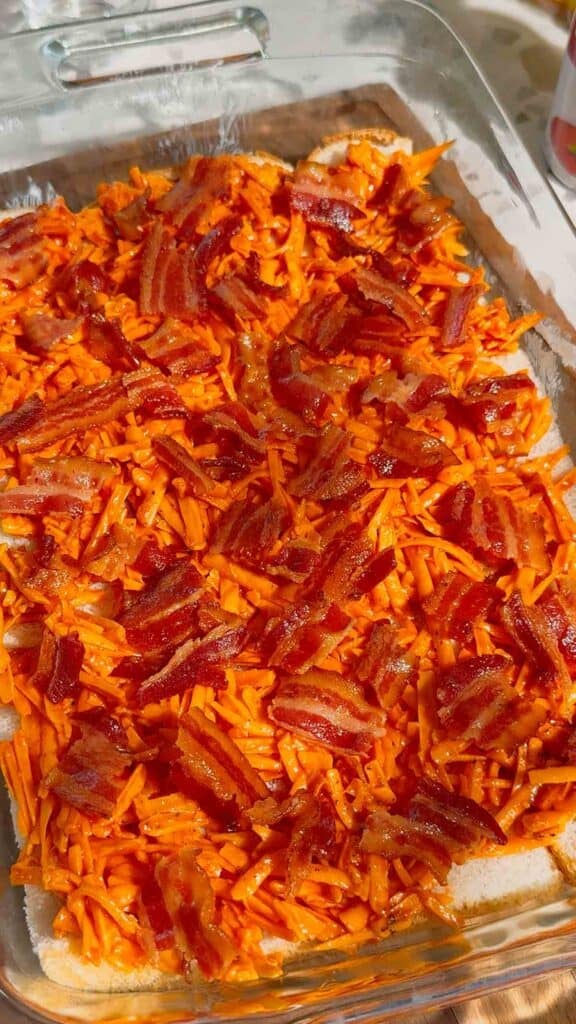 chopped bacon and shredded cheddar cheese mixture on top of bread in a casserole dish