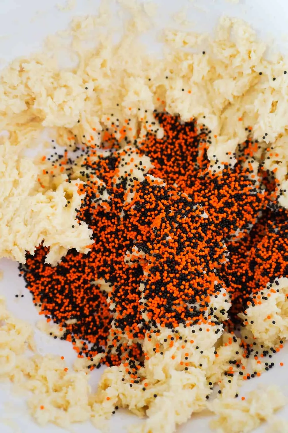 orange and black sprinkles added to sugar cookie dough in mixing bowl