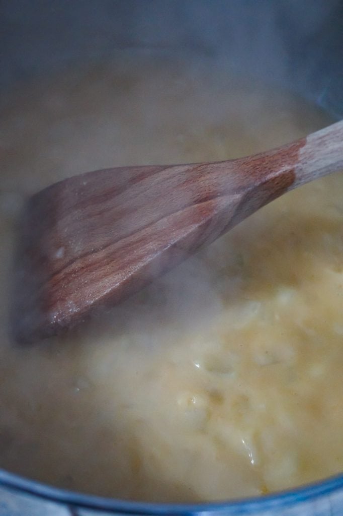 chicken broth added to cooked flour and onions in a pot with a wooden spoon