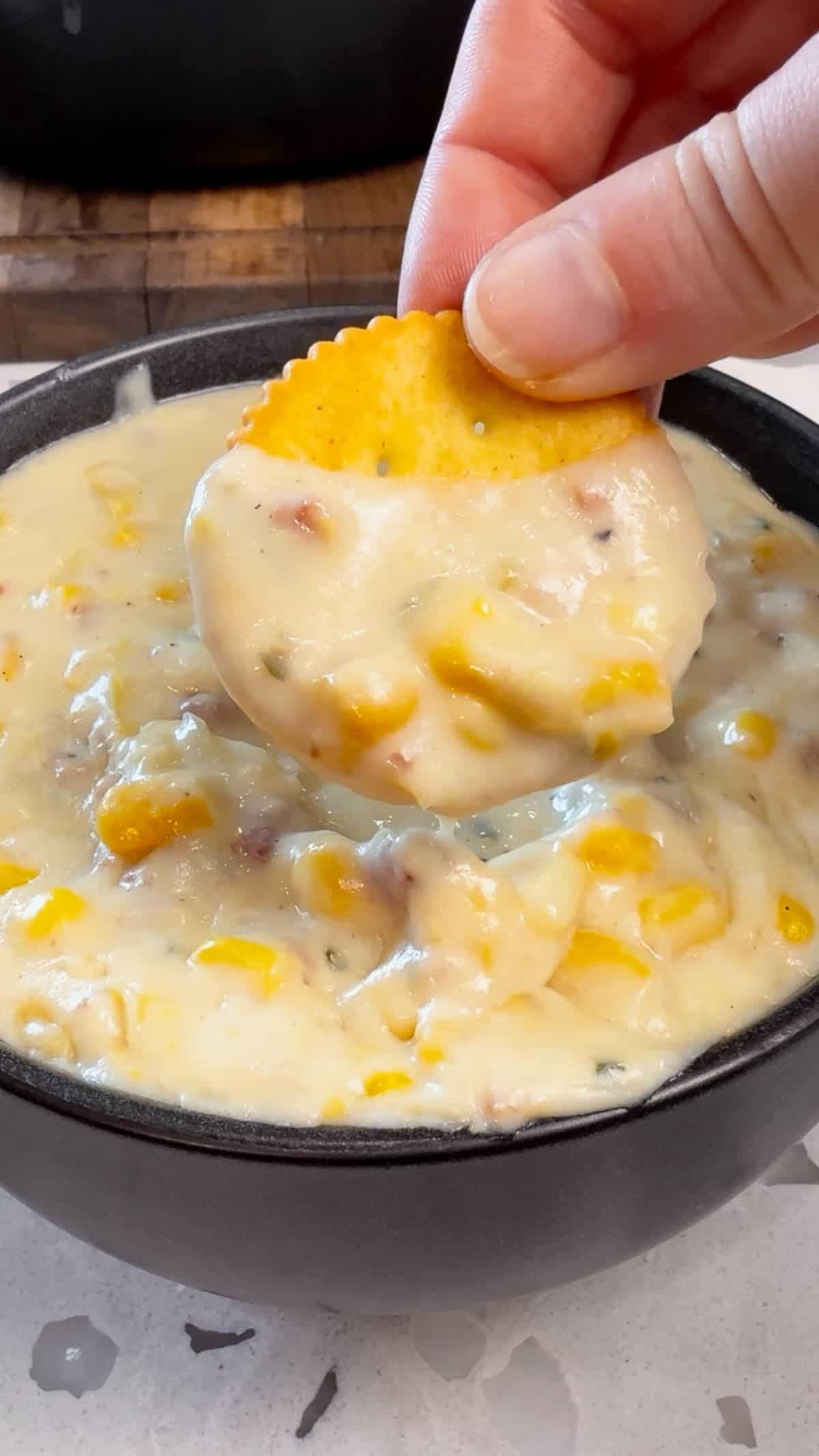 Ritz cracker being dipped in creamy corn chowder with bacon