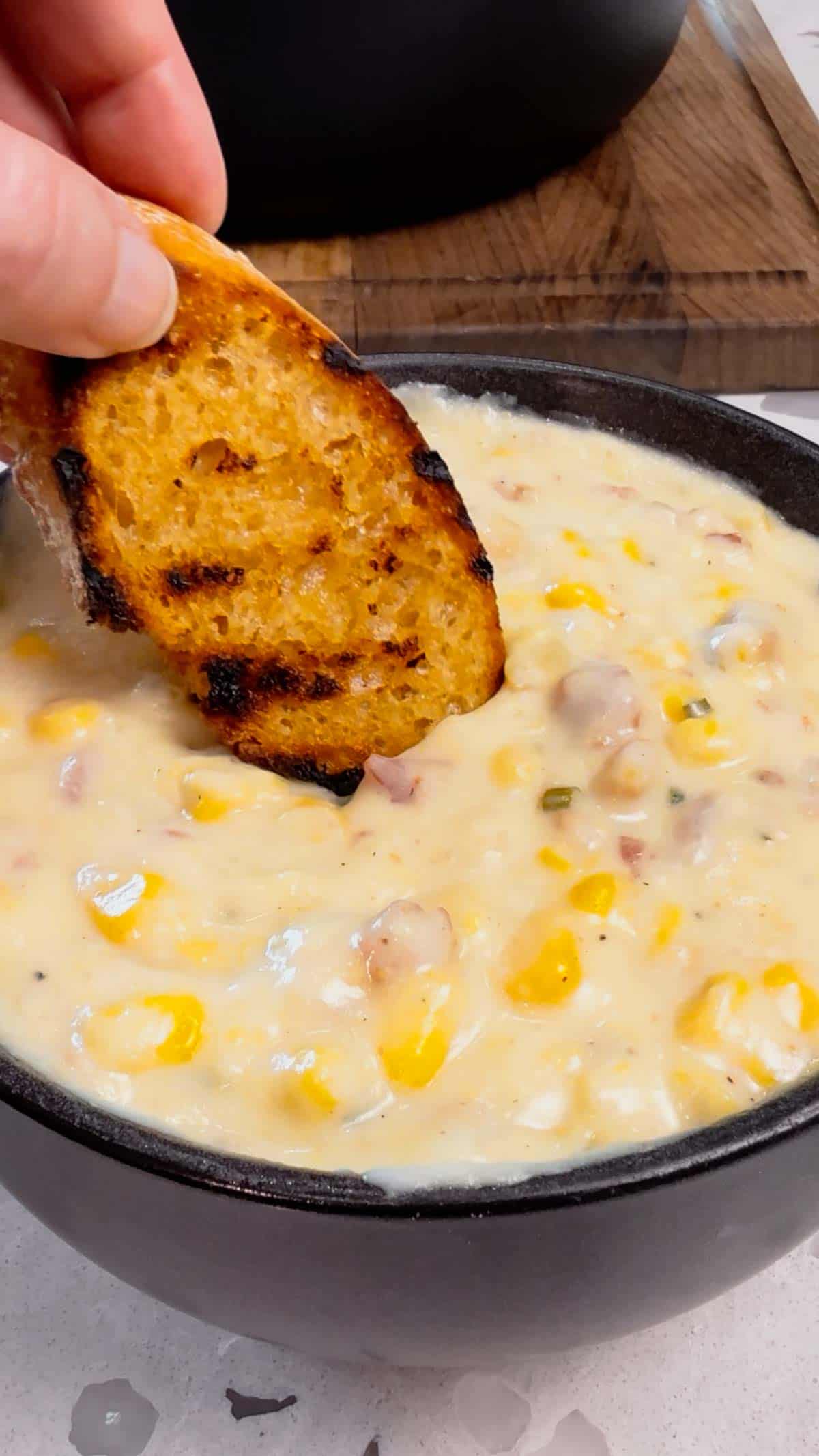baguette slice being dipped in creamy corn chowder