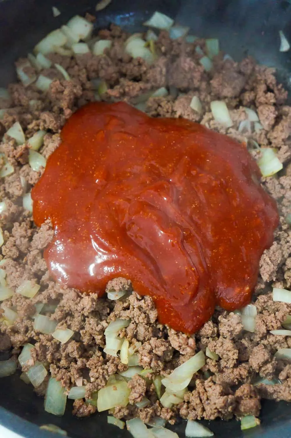 sloppy joe sauce on top of ground beef in a frying pan