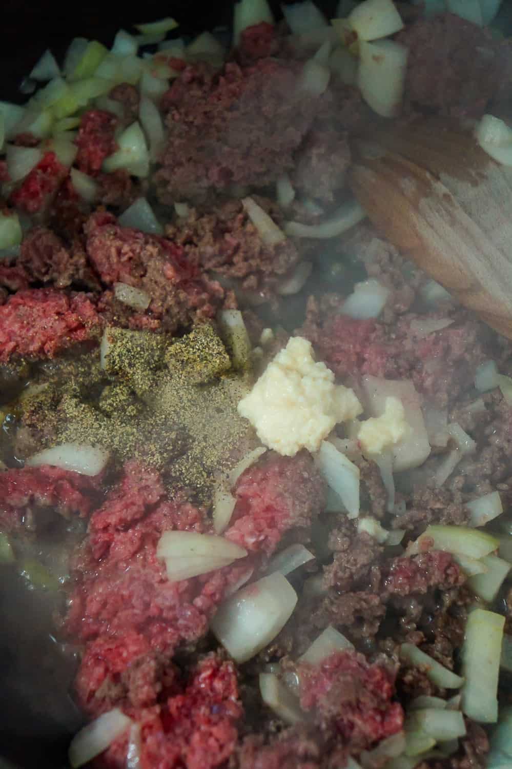 ground beef cooking in a frying pan with salt, pepper and garlic puree