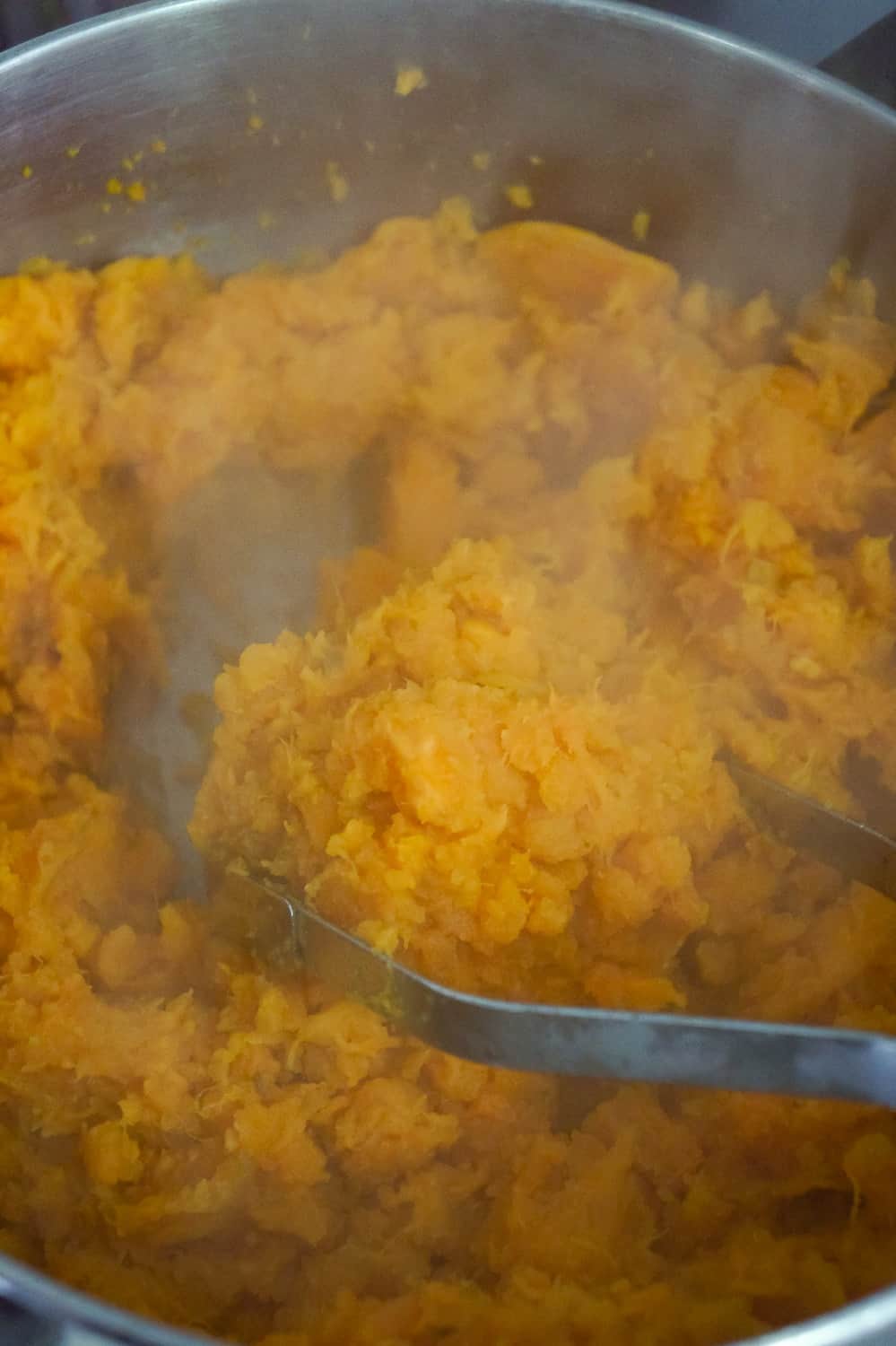 mashed sweet potatoes in a pot with a potato masher