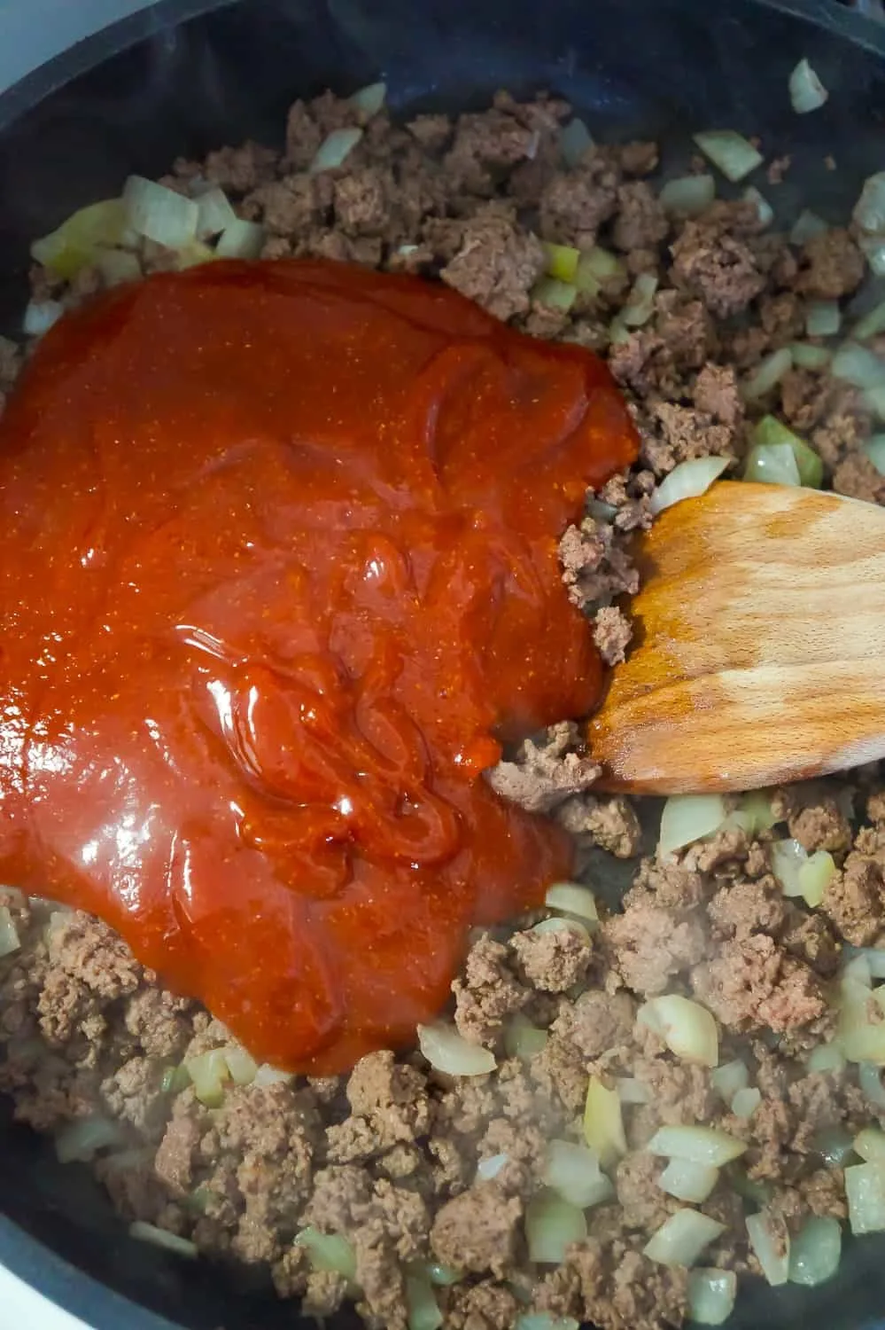 sloppy joe sauce added to cooked ground beef in a frying pan