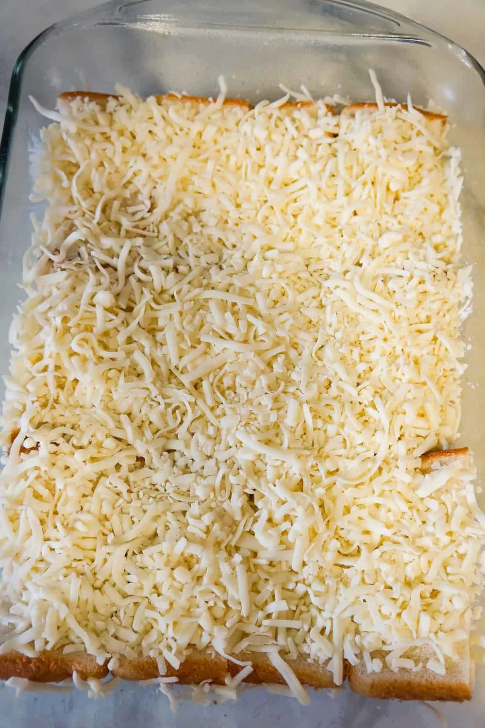 shredded mozzarella cheese on top of bread in a baking dish