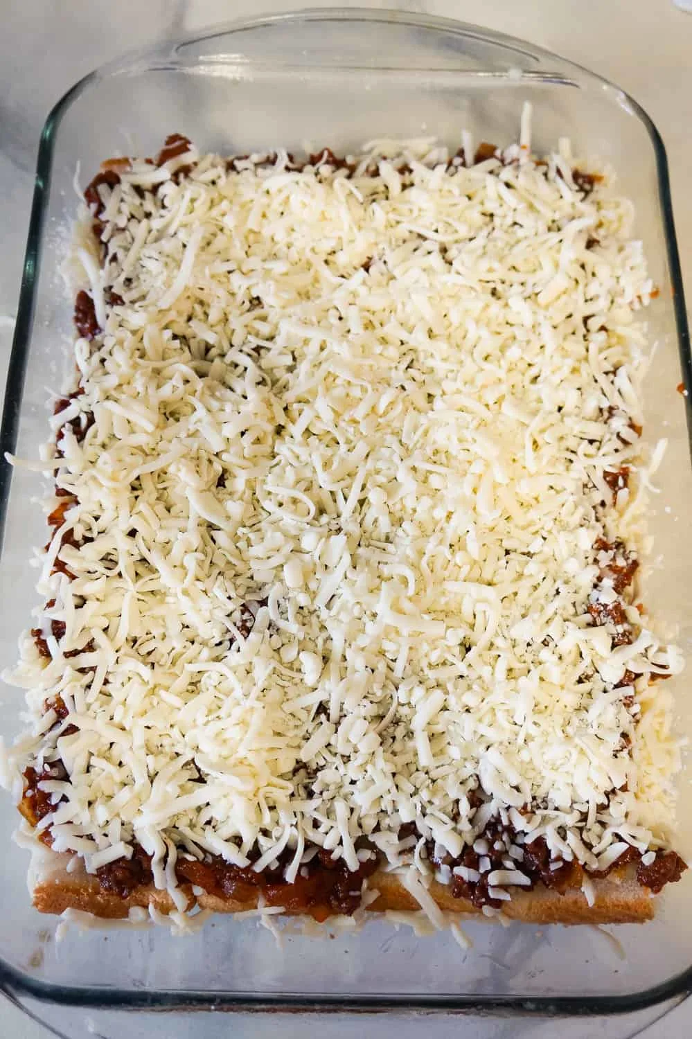 shredded mozzarella cheese on top of sloppy joe mixture in a baking dish