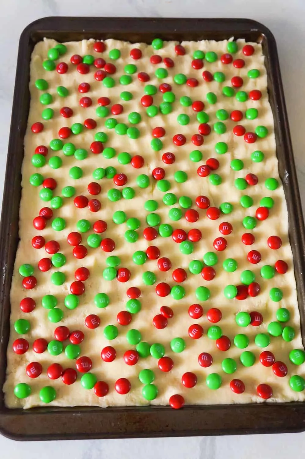 red and green M&M's on top of sugar cookie dough on a baking sheet