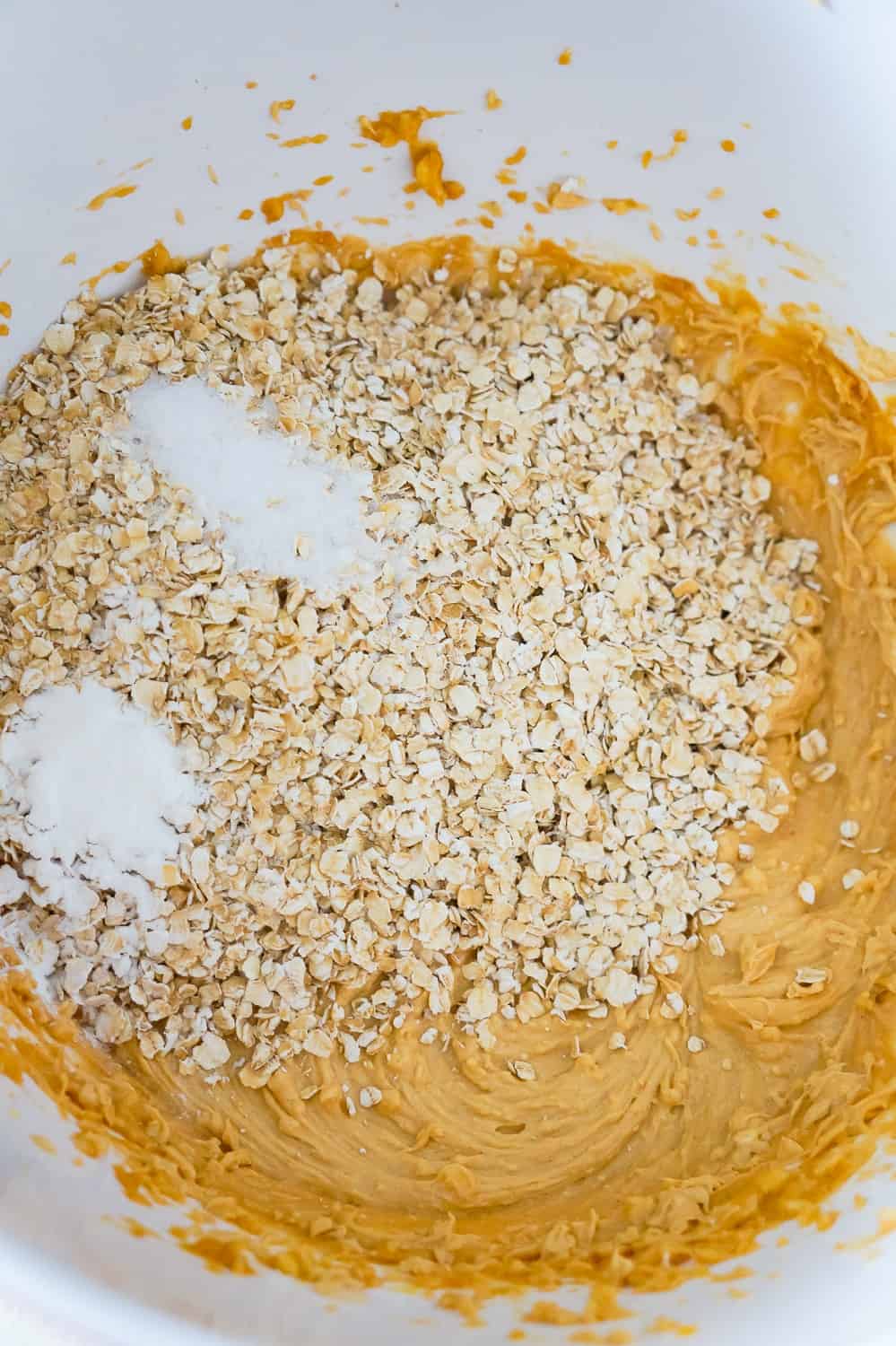quick oats, baking powder and salt on top of a peanut butter mixture in a mixing bowl