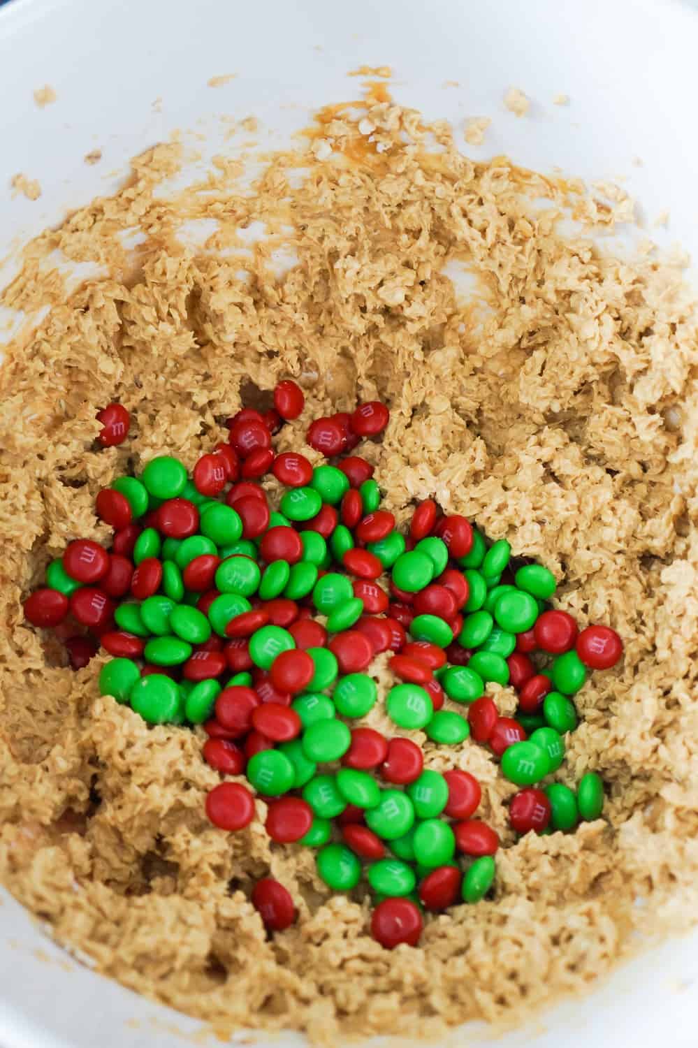 red and green M&Ms on top of peanut butter oatmeal cookie dough in a mixing bowl