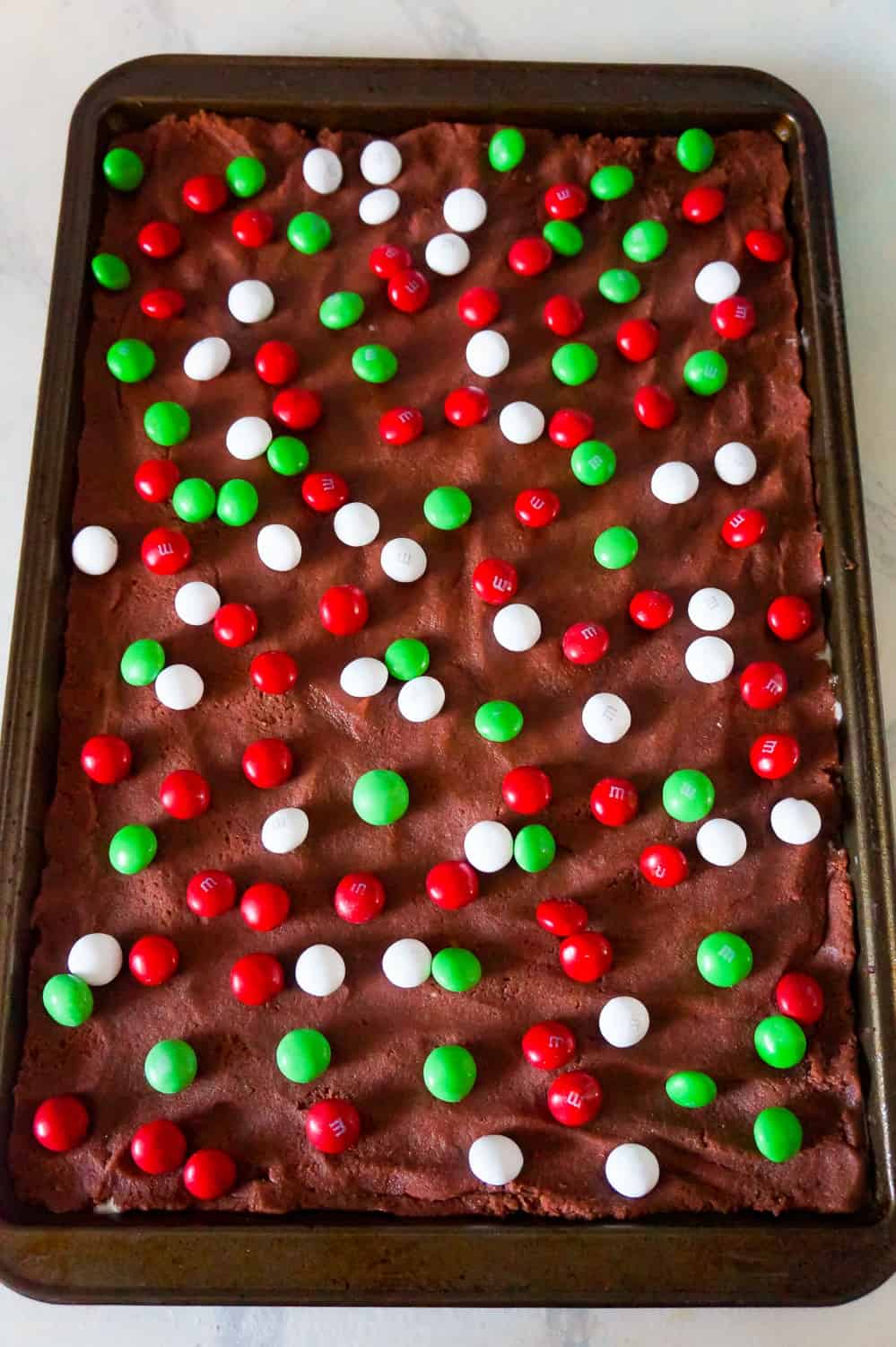 chocolate sugar cookie dough pressed out onto baking sheet with red, white and green M&Ms on top