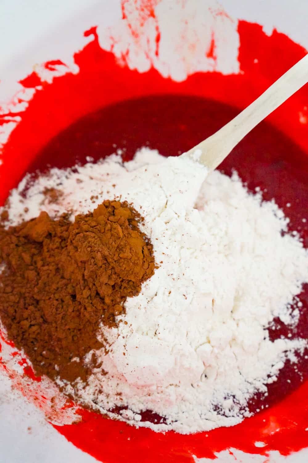 flour and cocoa powder on top of red batter in a mixing bowl