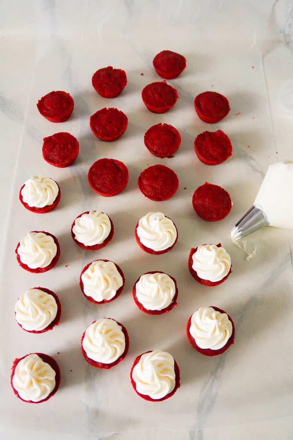 red velvet brownie bites being topped with cream cheese frosting