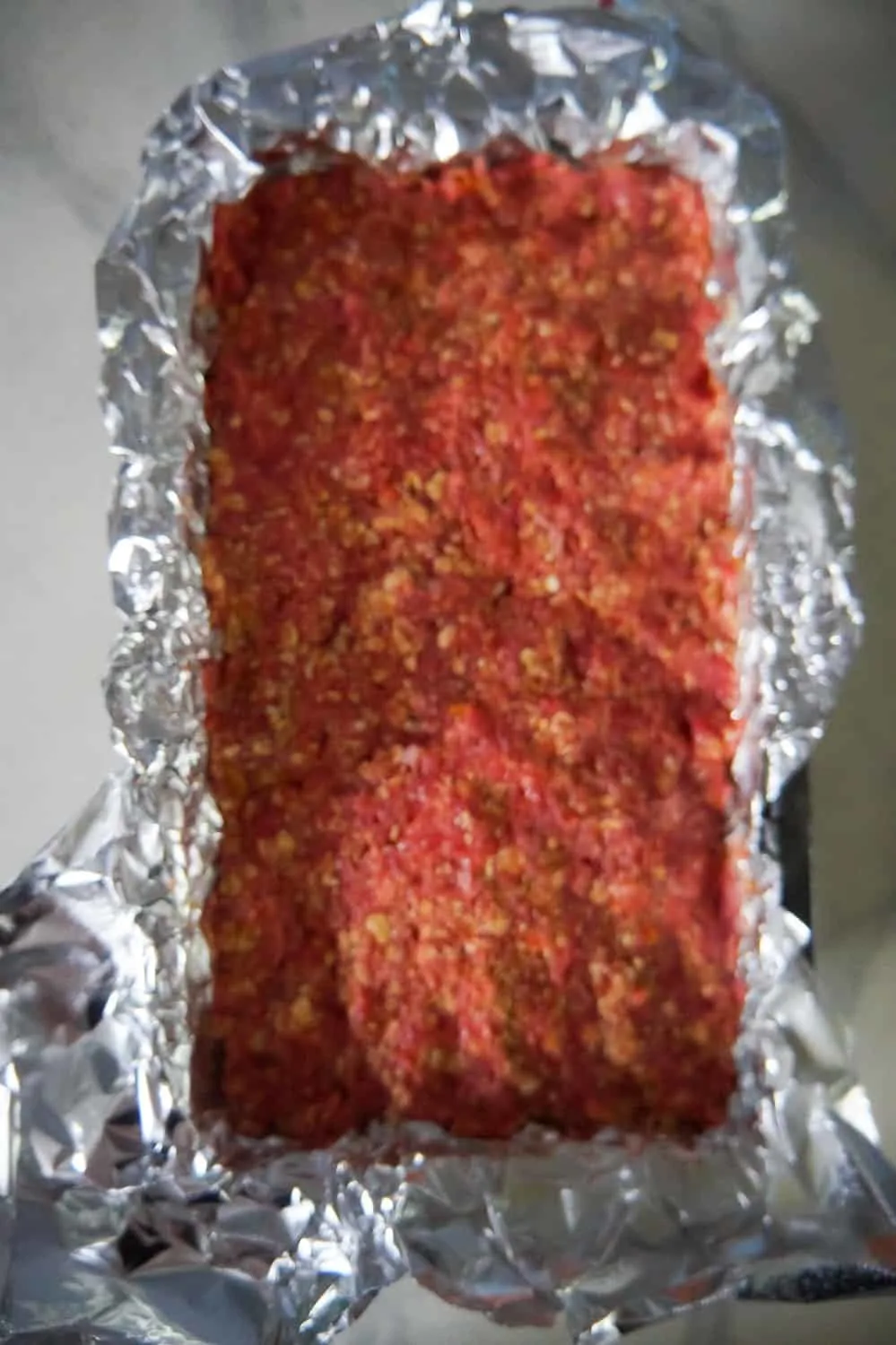 uncooked meatloaf in a loaf pan lined with aluminum foil