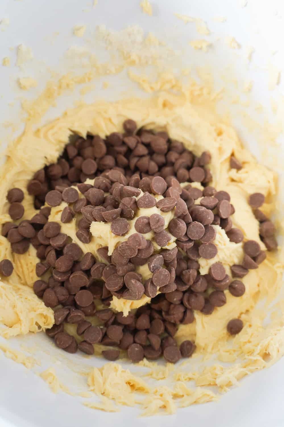 milk chocolate chips dumped on top of cake mix cookie dough in a mixing bowl