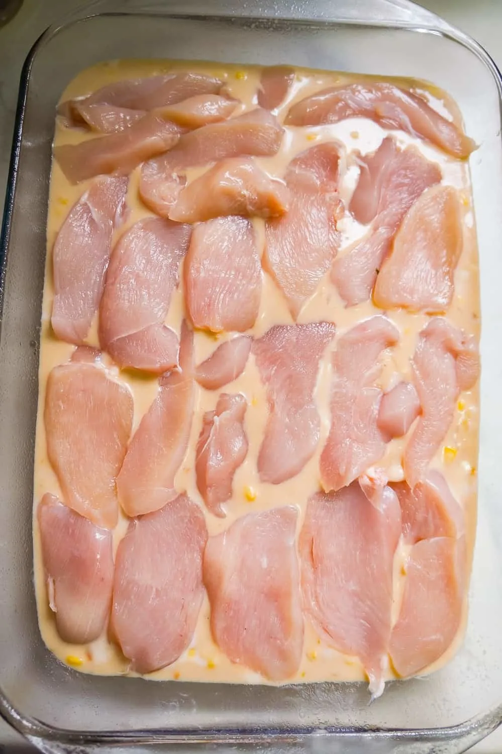 raw chicken breast slices on top of creamy rice mixture in a baking dish