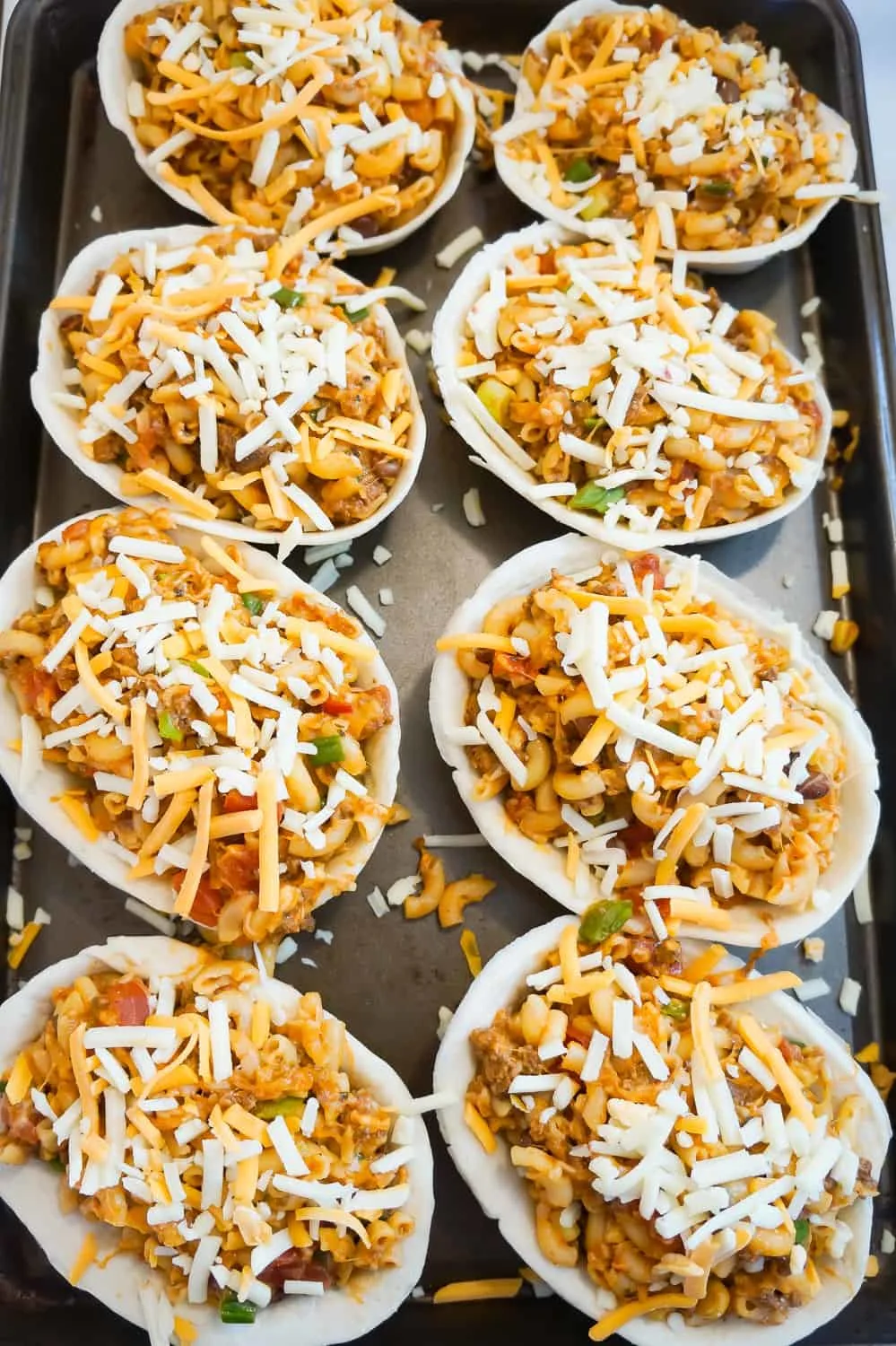 taco pasta topped with shredded cheese in tortilla bowls in a baking sheet