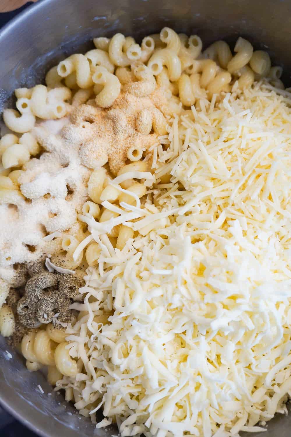 shredded cheese and spices on top of cavatappi pasta in a large pot
