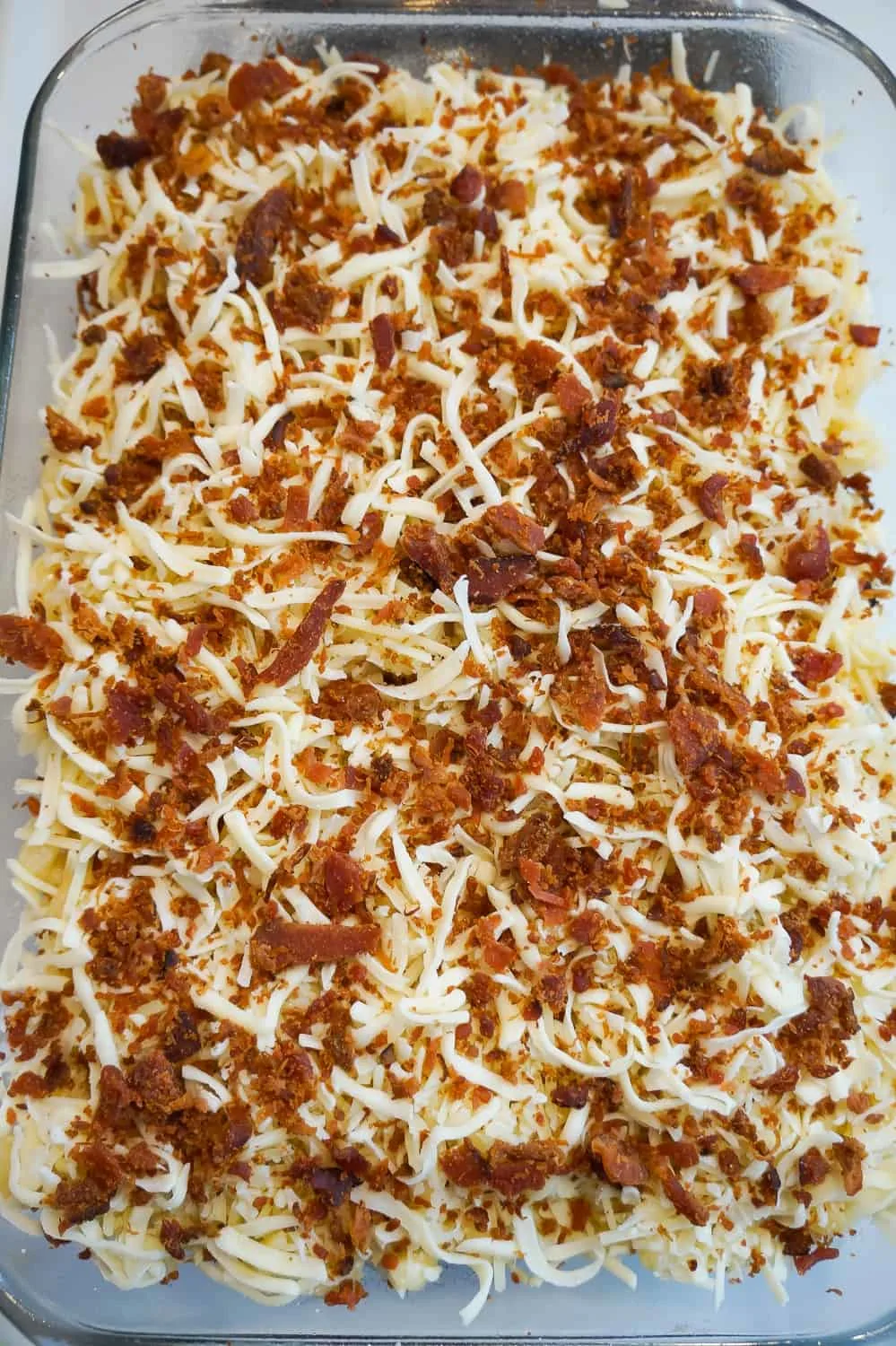 shredded Parmesan, shredded mozzarella and crumbled bacon on top of pasta in a baking dish