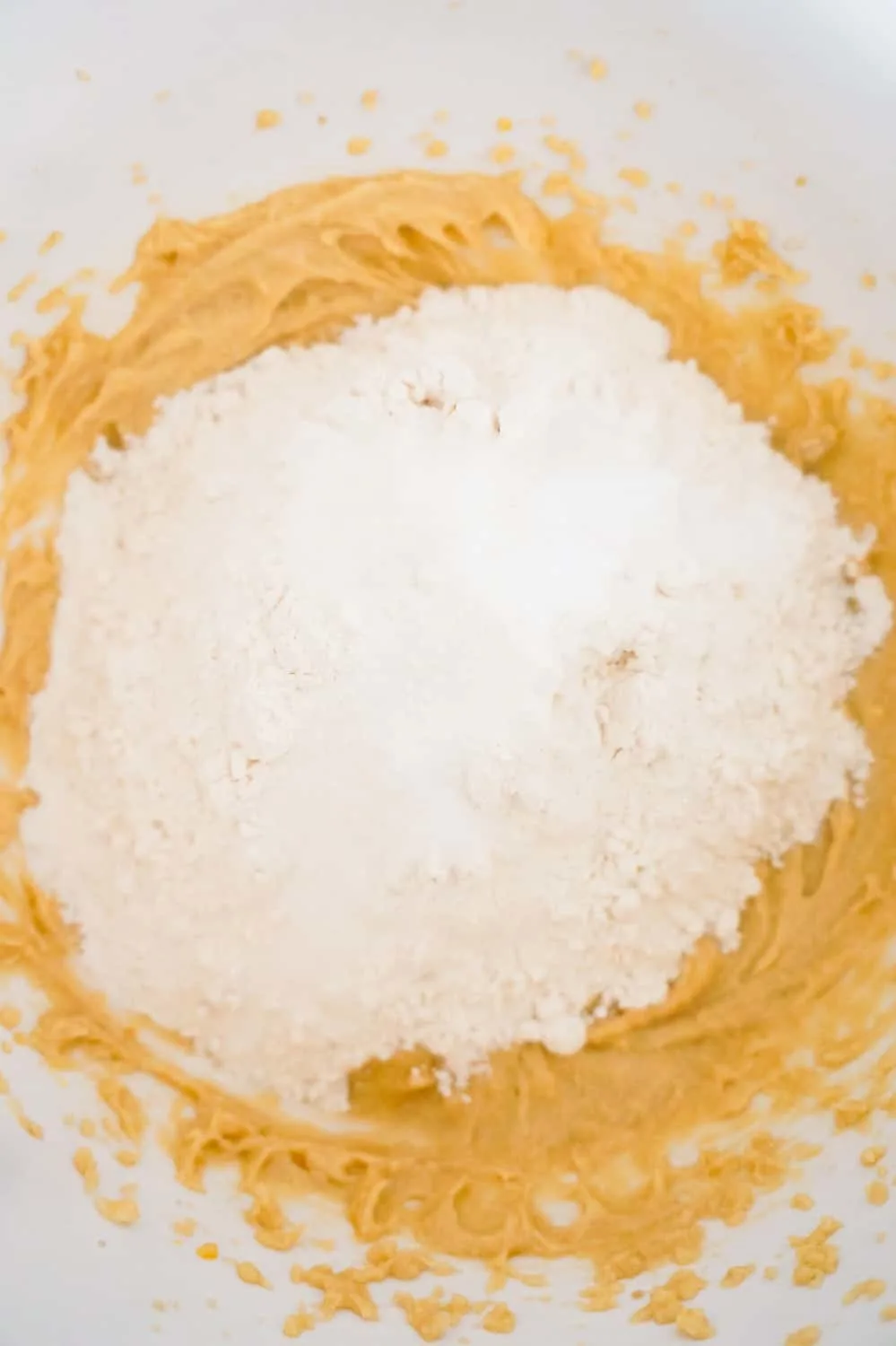 all purpose flour being added to cookie dough in a mixing bowl