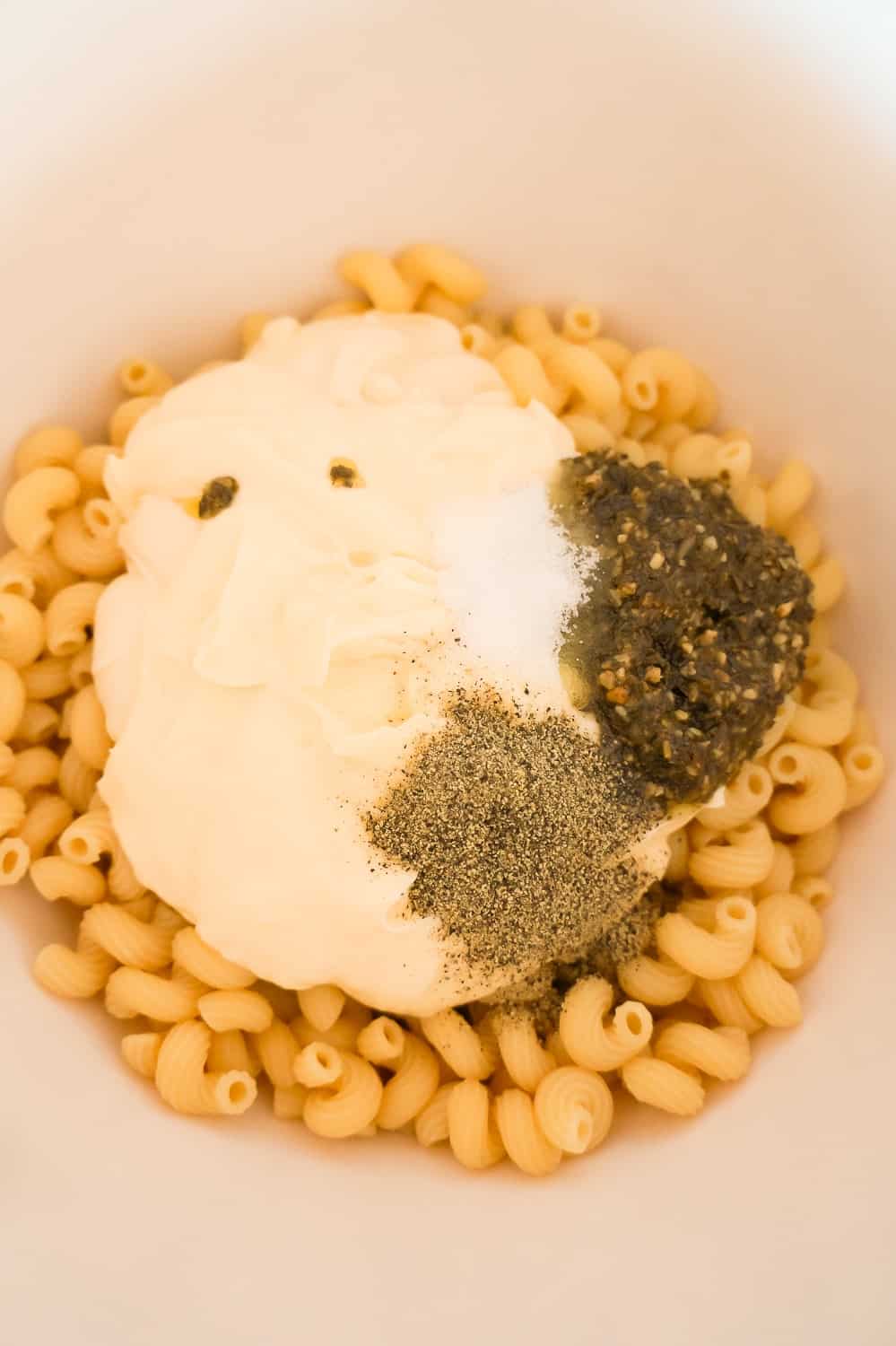 mayo, basil pesto, salt and pepper on top of cooked cavatappi noodles in a mixing bowl