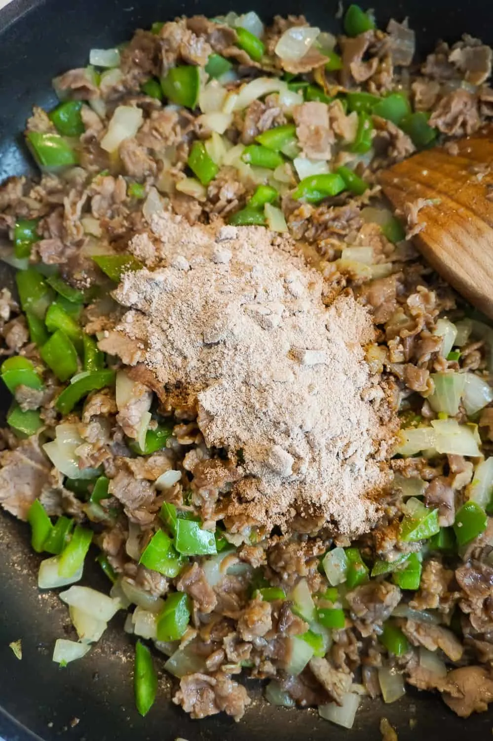 powdered gravy mix on top of diced roast beef and green peppers in a frying pan