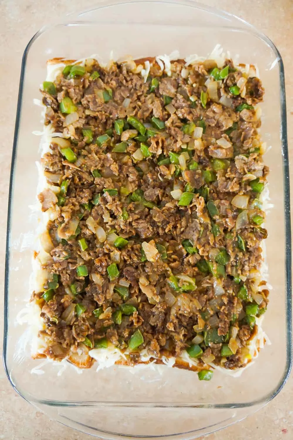 chopped roast beef and green pepper mixture on top of bread in a baking dish
