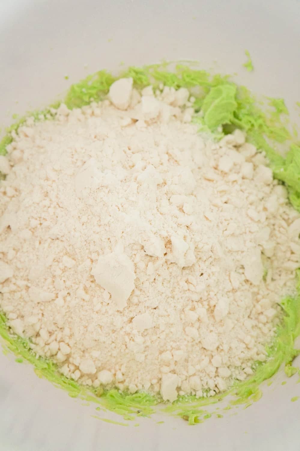 sugar cookie mix on top of pistachio pudding mixture in a mixing bowl