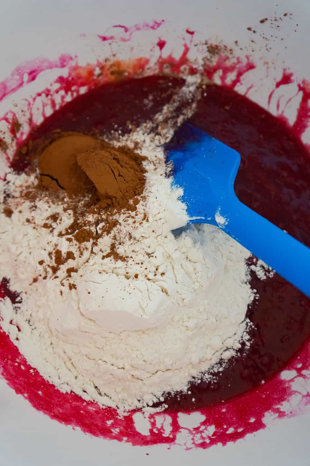 flour and cocoa powder added to red velvet brownie batter in a mixing bowl