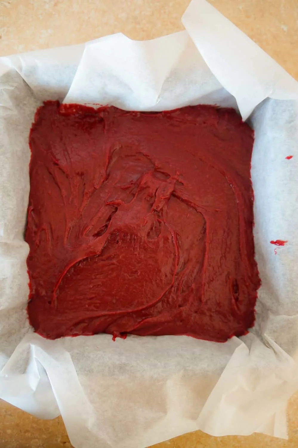 red velvet brownie batter in a parchment lined baking pan