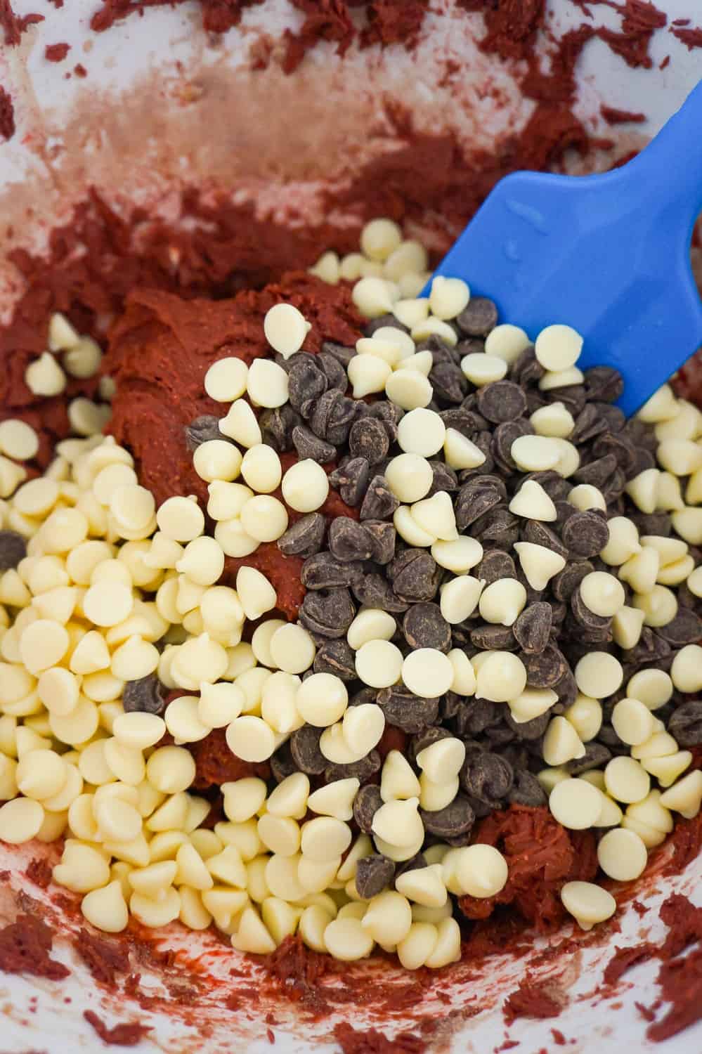 white chocolate chips and semi sweet chocolate chips on top of red velvet cookie dough in a mixing bowl