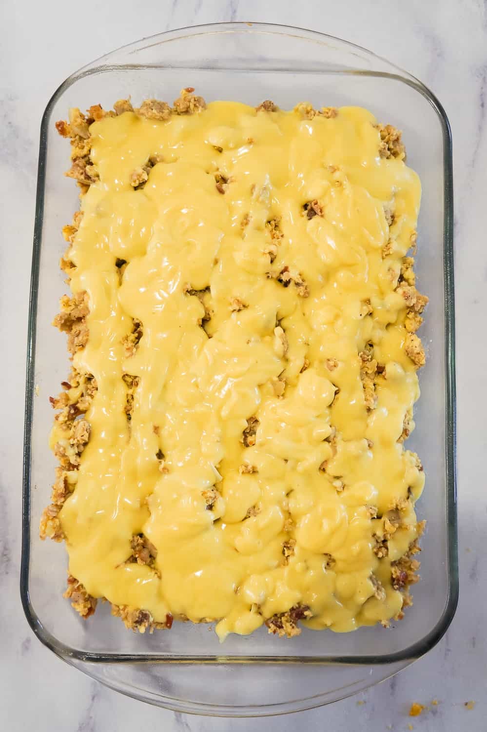 Hollandaise sauce poured over egg and sausage mixture in a baking dish