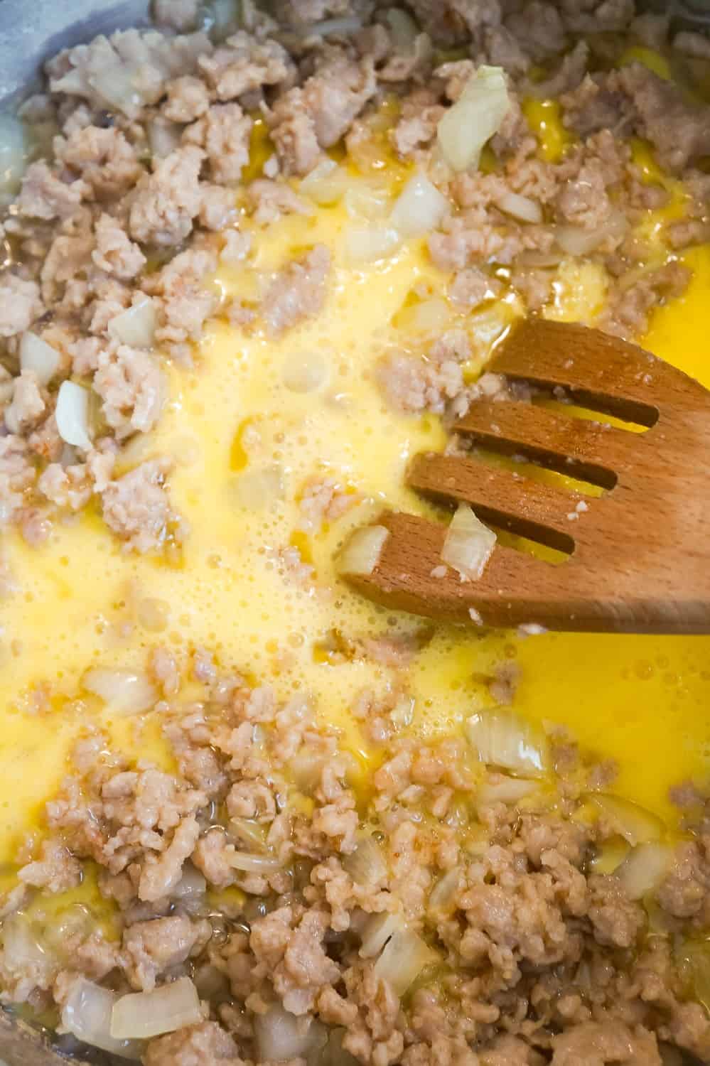 beaten eggs added to cooked sausage meat in a pan