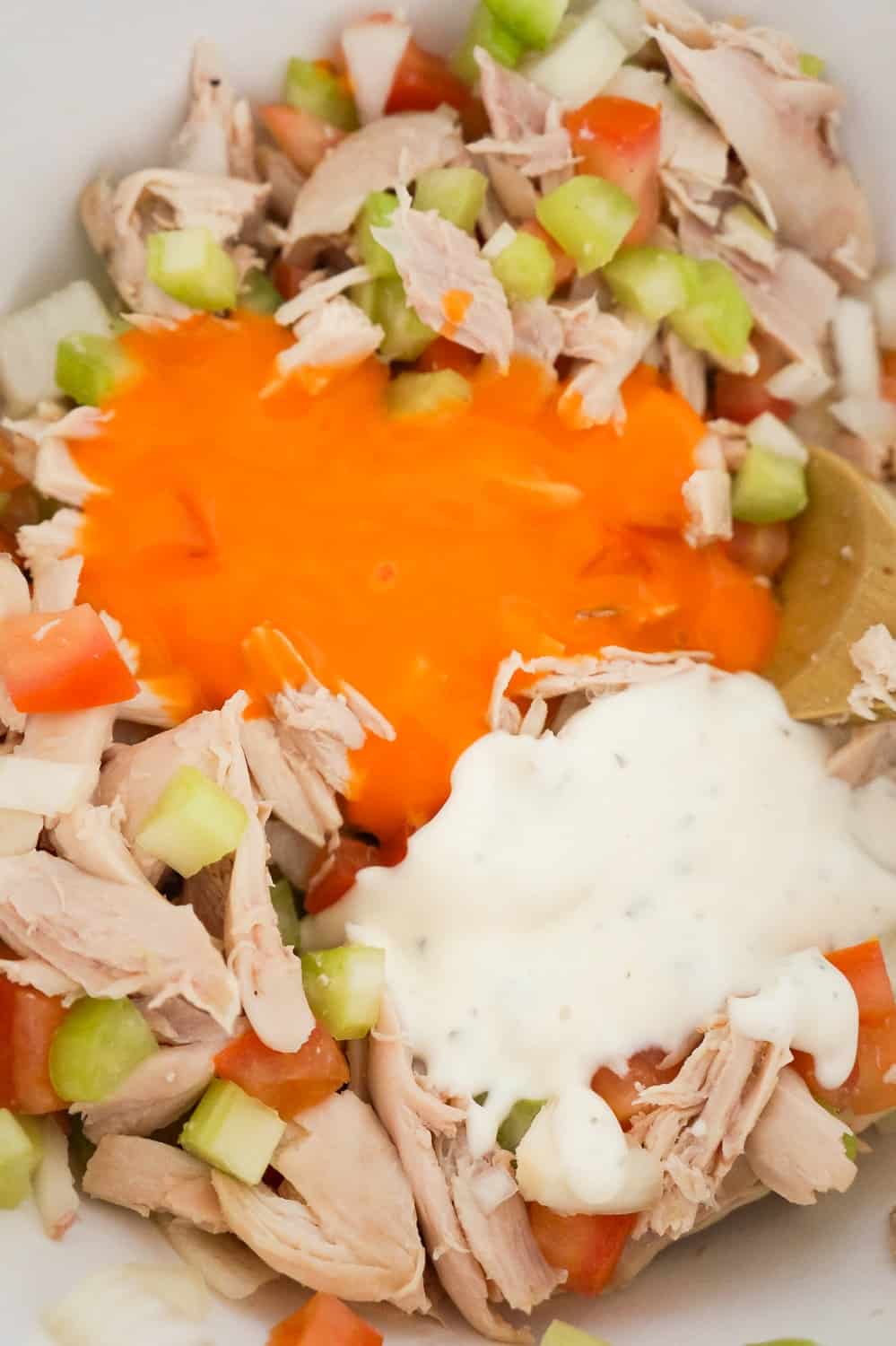 buffalo sauce and ranch dressing on top of shredded chicken and diced vegetables in a mixing bowl