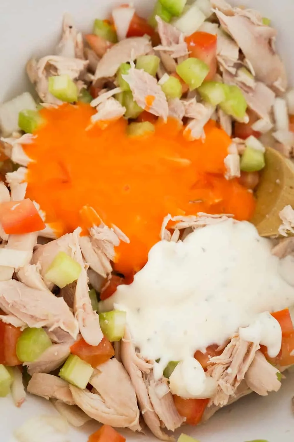 buffalo sauce and ranch dressing on top of shredded chicken and diced vegetables in a mixing bowl