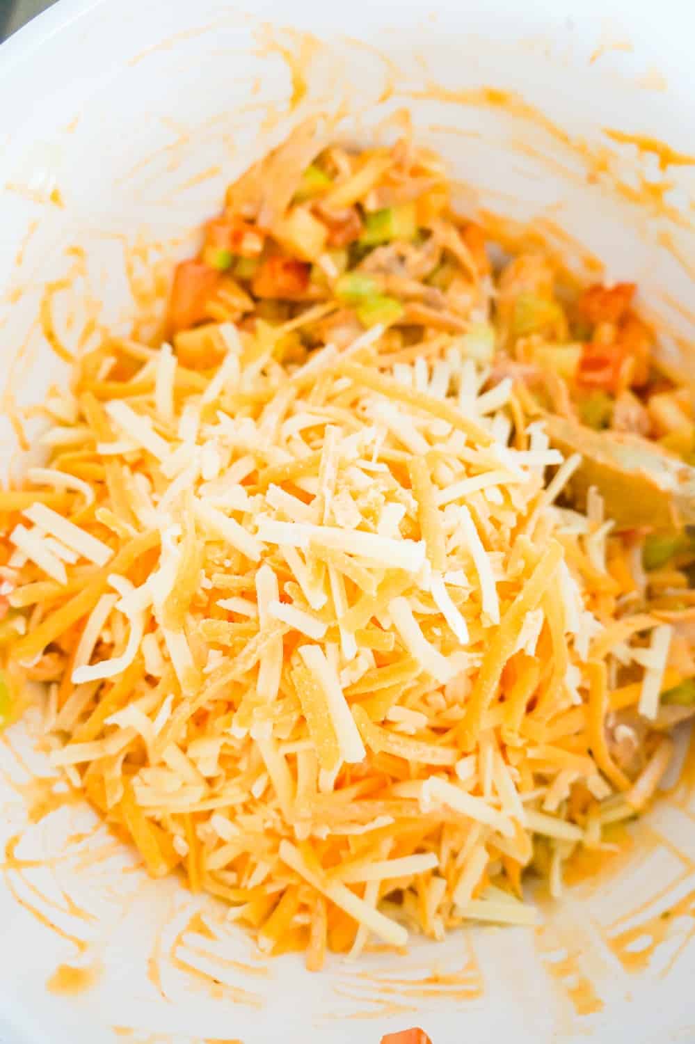 shredded cheddar cheese on top of buffalo chicken mixture in a mixing bowl