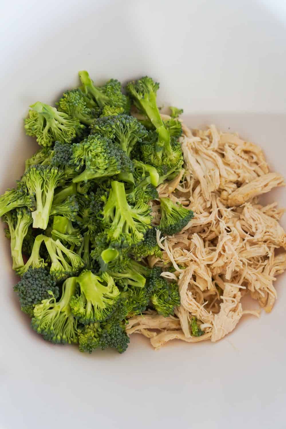 broccoli florets and shredded chicken in a mixing bowl