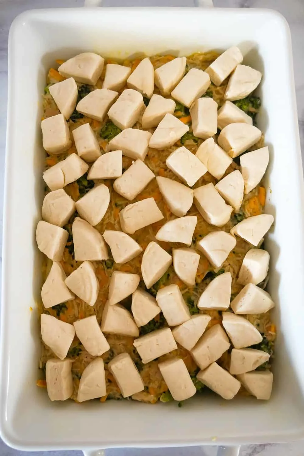 biscuit dough pieces on top of chicken and broccoli mixture in a baking dish