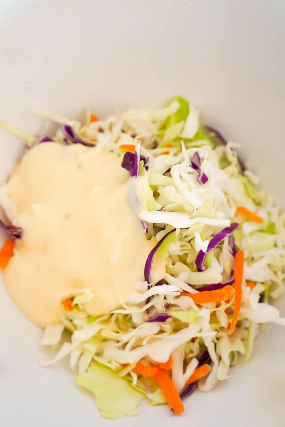 shredded coleslaw mix and creamy coleslaw dressing in a mixing bowl