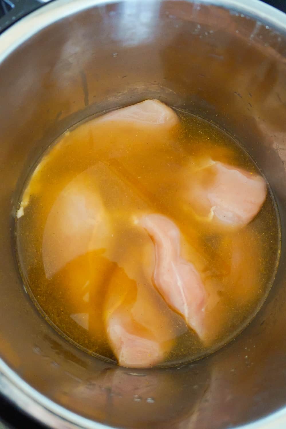 Raw chicken breast in liquid in an Instant Pot