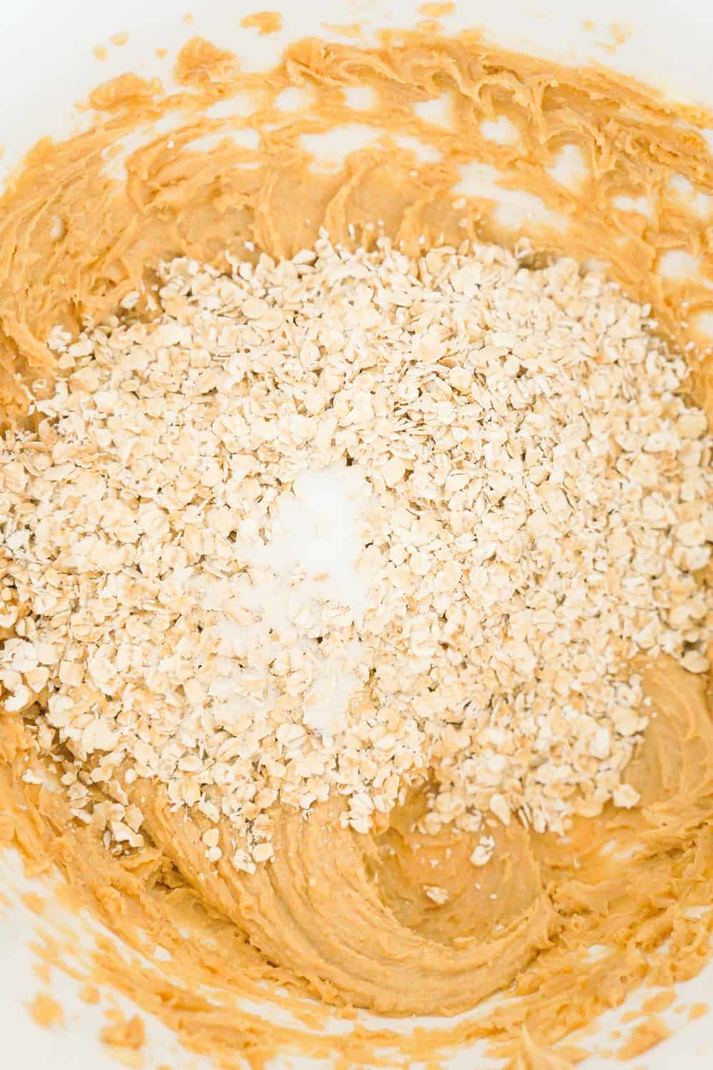 quick oats and salts on top of creamy peanut butter mixture in a bowl