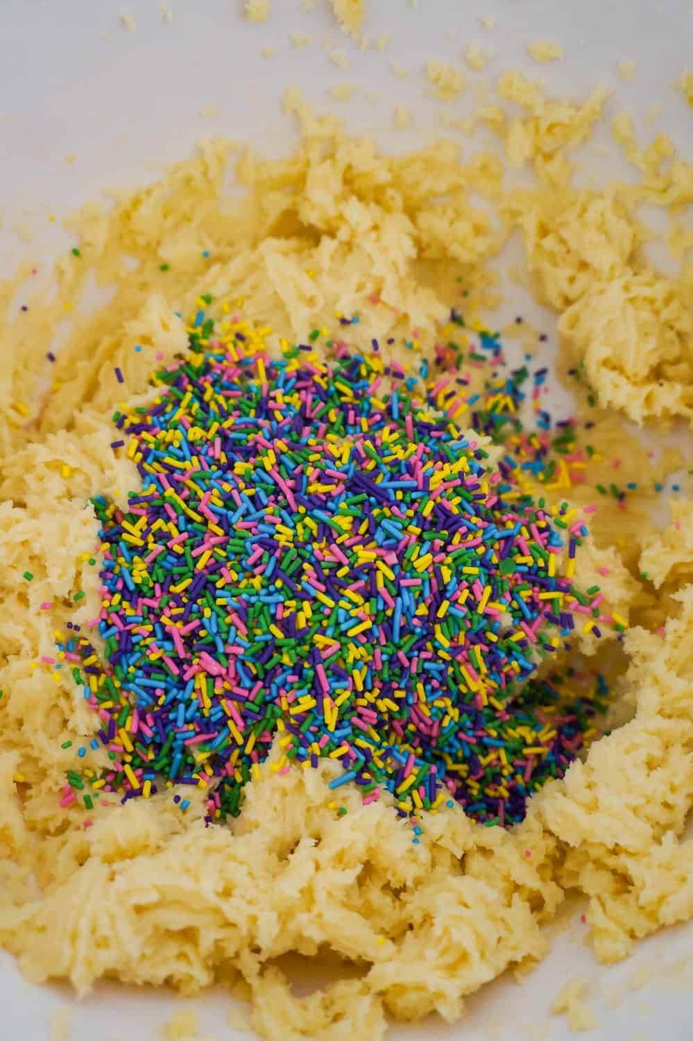 colourful sprinkles on top of sugar cookie dough in a mixing bowl